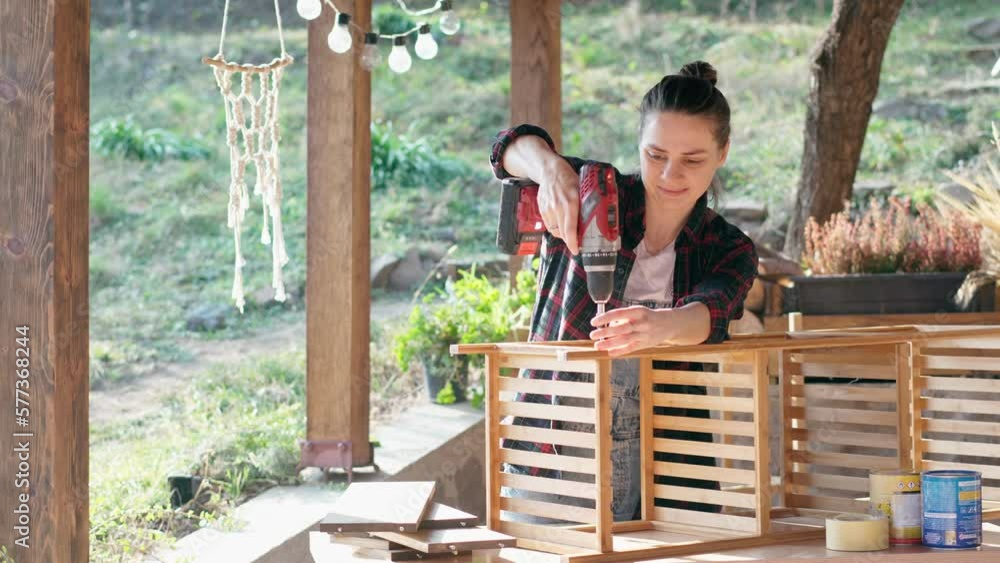 A woman doing DIY work at home. A female using an electric screwdriver to assemble a wooden shelf outdoors. A woman doing DIY work at home. A female using an electric screwdriver to assemble a wooden shelf outdoors.