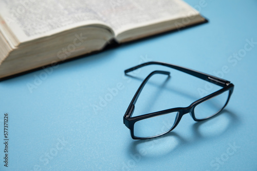 Eyeglasses and book on the blue background.