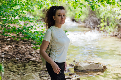a woman with a backpack stands by the river in the woods walking the hike