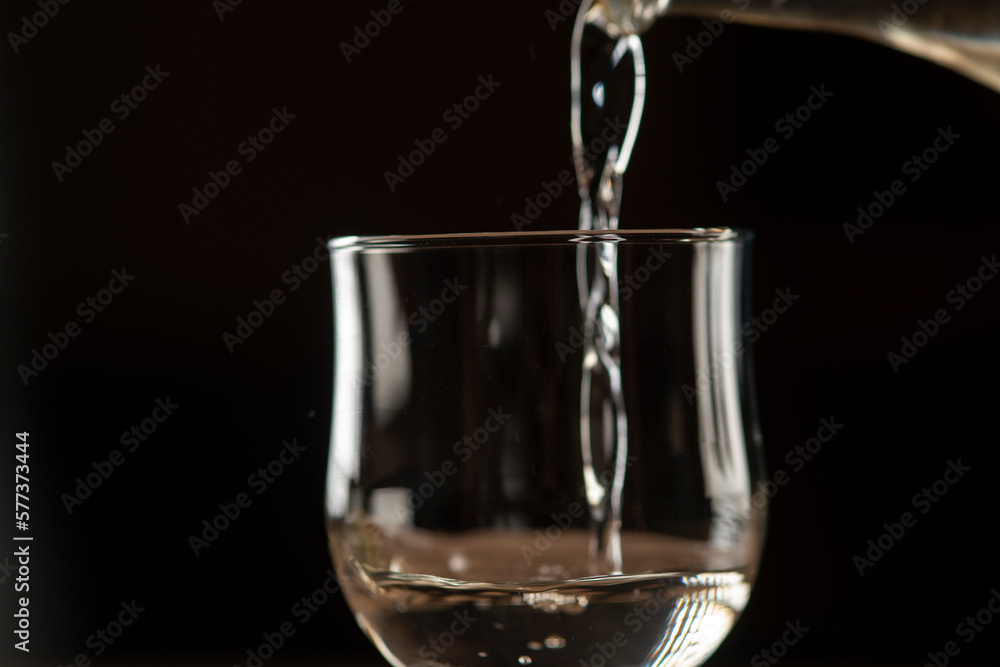 girl hands pouring red wine into a glass from a clay bottle on a black background girl hands pouring red wine into a glass from a clay bottle on a black background
