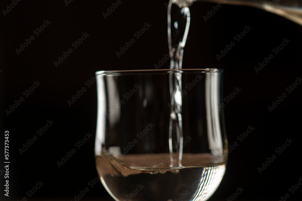 girl hands pouring red wine into a glass from a clay bottle on a black background