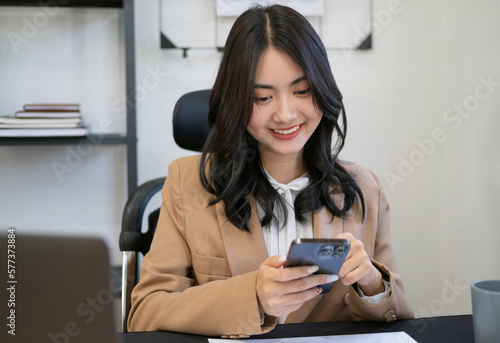 Young business woman on the phone at office. Business woman texting on the phone and working on laptop. Pretty young business woman sitting on workplace. Smiling business woman.