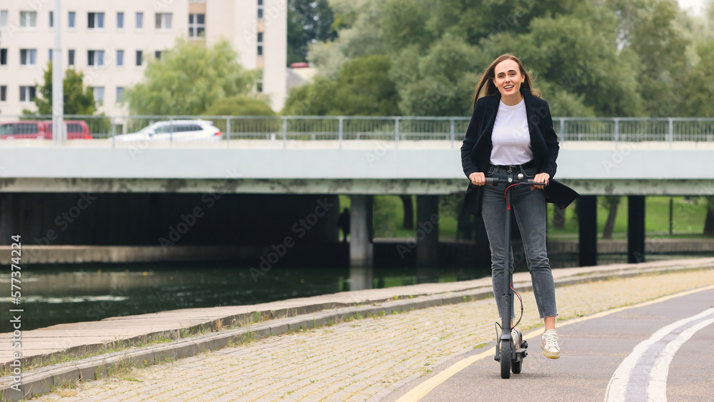 A young woman in stylish clothes rides an electric scooter on a bike path.Urban infrastructure