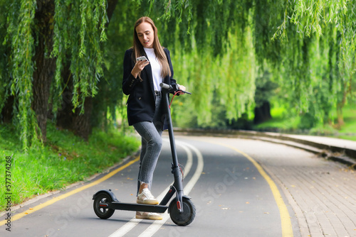 A young woman is typing on her phone while riding a scooter. Hipster on eco transport