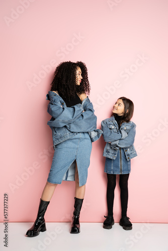 Full length of trendy preteen kid and mom looking at each other on pink background.