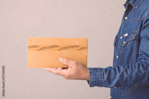 Man holding brown confidential envelope sealed with tape and word Please do not accept if seal is broken in Thai and English. photo