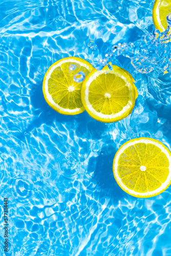 Creative summer composition made of sliced lemon in transparent blue water. Refreshment concept. Healthy refreshing drink theme. Top view
