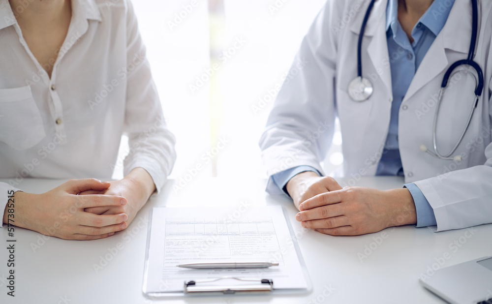 Doctor and patient discussing current health questions while sitting near of each other and using clipboard at the table in clinic, just hands closeup. Medicine concept. Doctor and patient discussing current health questions while sitting near of each other and using clipboard at the table in clinic, just hands closeup. Medicine concept.
