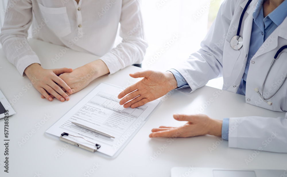 Doctor and patient discussing current health questions while sitting near of each other and using clipboard at the table in clinic, just hands closeup. Medicine concept. Doctor and patient discussing current health questions while sitting near of each other and using clipboard at the table in clinic, just hands closeup. Medicine concept.