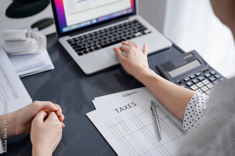 Woman accountant using a calculator and laptop computer while counting taxes for a client. Business audit and finance concepts. Woman accountant using a calculator and laptop computer while counting taxes for a client. Business audit and finance concepts.