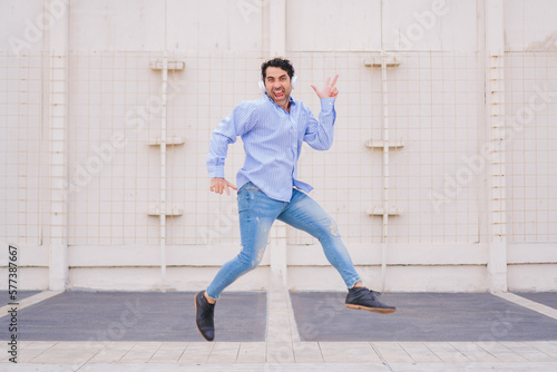 Middle-aged latin man with headphones jumping happily with ecstatic expression.