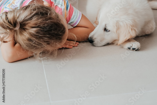sad along child toddler girl puppy pet dog Golden Retriever lie together on floor copy space friendship white beige natural pastel colores porcelain floor tile. loneliness pet therapy and canisterapy