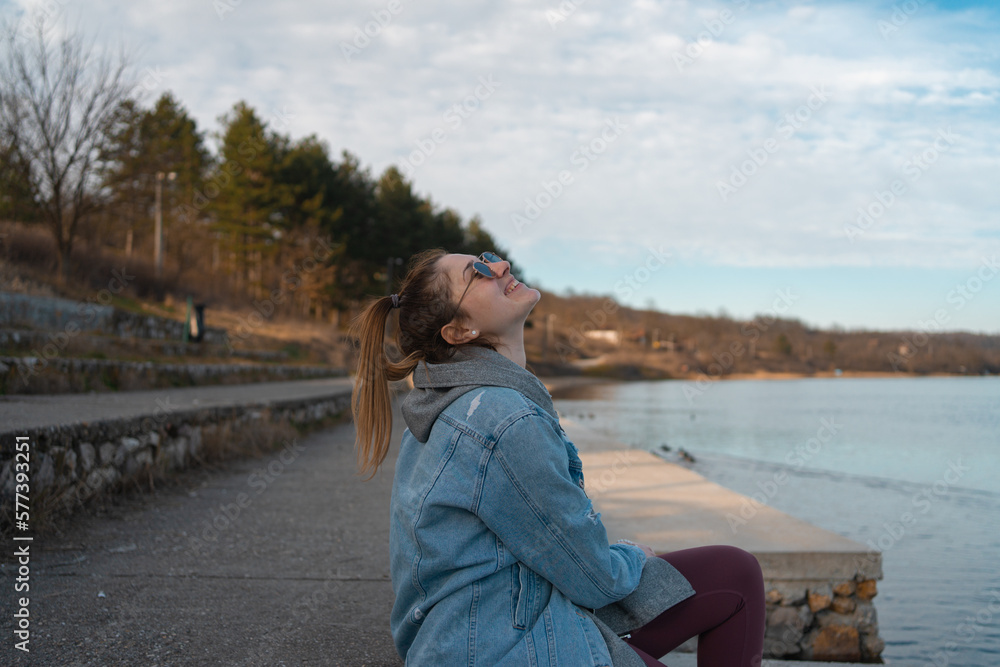 Young woman sits on the shore of the lake, enjoying in her free time. Young woman sits on the shore of the lake, enjoying in her free time.