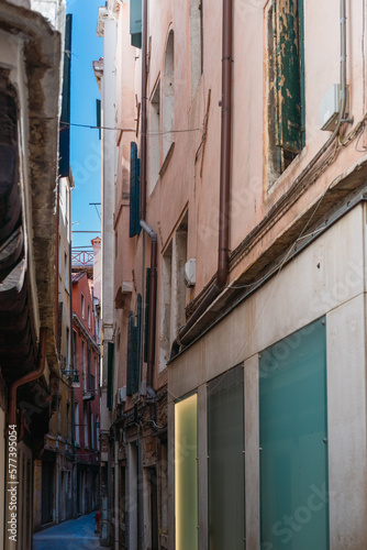 View of a narrow street in Venice with a strip of blue sky in the background on a sunny day, old vintage walls of authentic houses, Italian medieval architecture, Venice culture, tourist attractions © Александр Бочкала