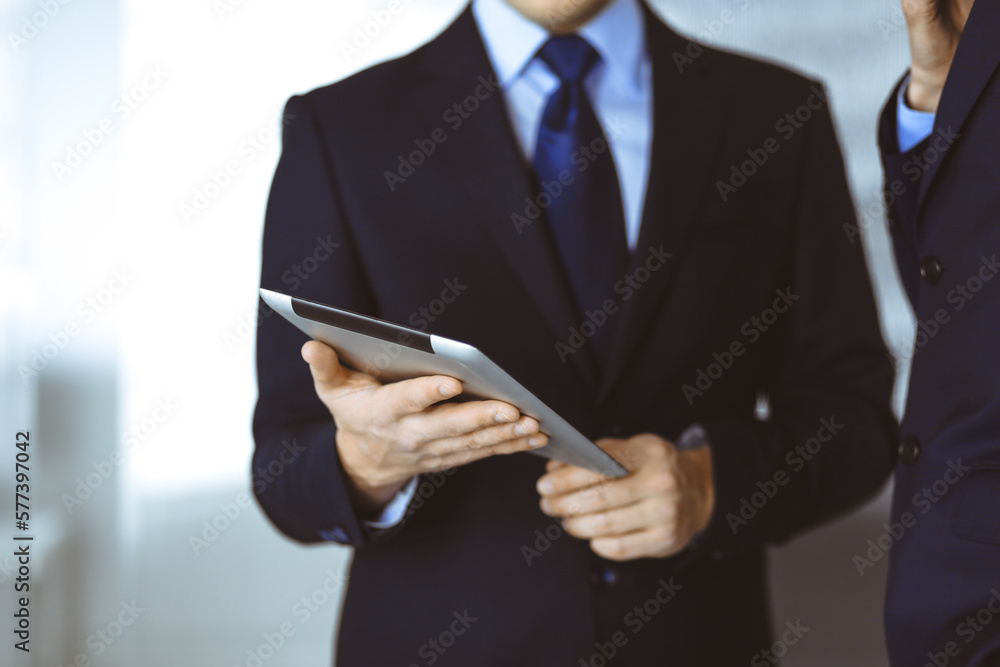 Business people use a tablet computer for discussion of their new project, standing in a modern office. Unknown businessman or male entrepreneur with a colleague at workplace Business people use a tablet computer for discussion of their new project, standing in a modern office. Unknown businessman or male entrepreneur with a colleague at workplace