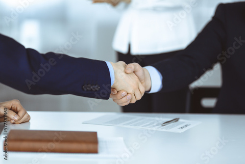Business people shaking hands at meeting or negotiation, close-up. Group of unknown businessmen, and a woman on the background in a modern office. Teamwork, partnership and handshake concept.