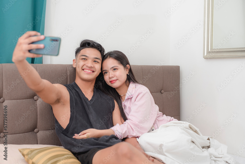 A man takes a selfie with his girlfriend while vacationing in a hotel bedroom. A man takes a selfie with his girlfriend while vacationing in a hotel bedroom.
