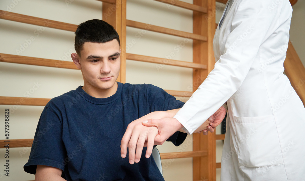 Obraz premium Young doctor neurologist examining her patient. Pretty female orthopedist with patient in her office. Neurologist checks the reflexes of a young age male patient.