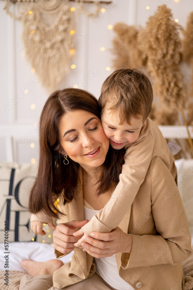 happy mom hugs and kisses a small child on the bed in beige brown natural tones, having fun happy mom hugs and kisses a small child on the bed in beige brown natural tones, having fun