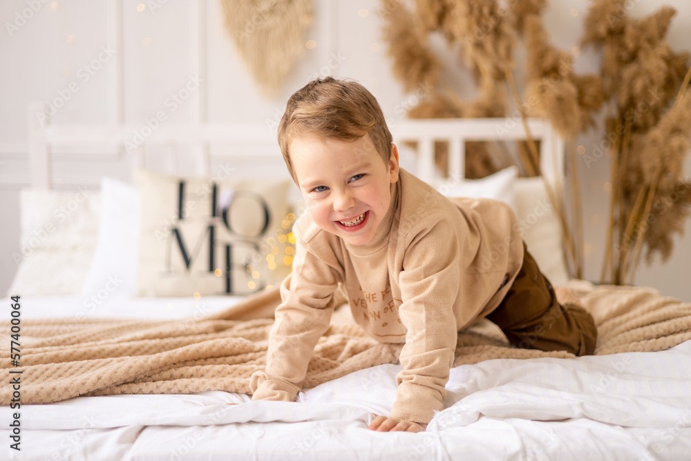 a small child on a bed in beige brown natural tones is laughing and rejoicing, a cheerful and funny little kid is playing at home a small child on a bed in beige brown natural tones is laughing and rejoicing, a cheerful and funny little kid is playing at home
