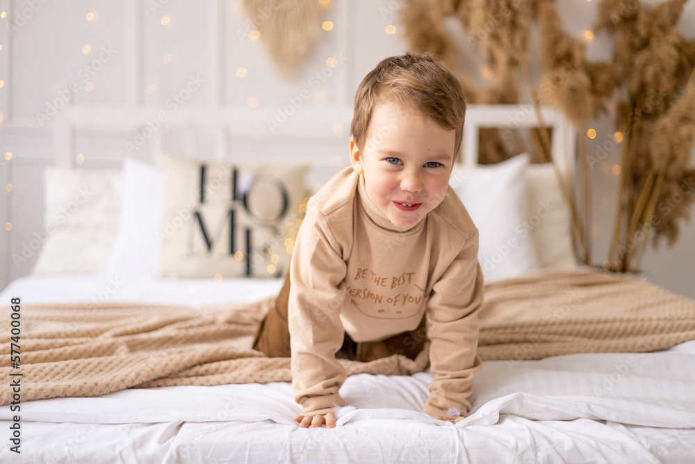 a small child on a bed in beige brown natural tones is laughing and rejoicing, a cheerful and funny little kid is playing at home a small child on a bed in beige brown natural tones is laughing and rejoicing, a cheerful and funny little kid is playing at home