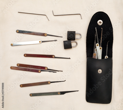 Many lock picking tools in a case, tension wrenches and 2 little padlocks flat lay. A kit of lock picks that can be used by a locksmith for opening doors or burglary