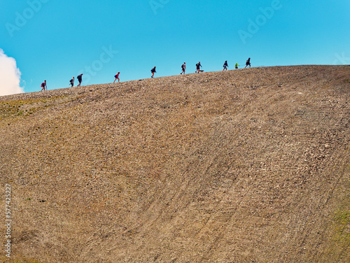 Fotografie Group of hikers walking on a mountain uphill in summer