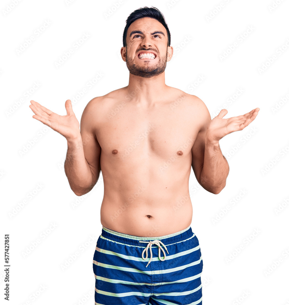 Young handsome man wearing swimwear crazy and mad shouting and yelling with aggressive expression and arms raised. frustration concept. Young handsome man wearing swimwear crazy and mad shouting and yelling with aggressive expression and arms raised. frustration concept.