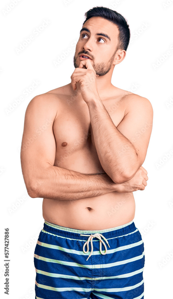 Fototapeta premium Young handsome man wearing swimwear with hand on chin thinking about question, pensive expression. smiling with thoughtful face. doubt concept.