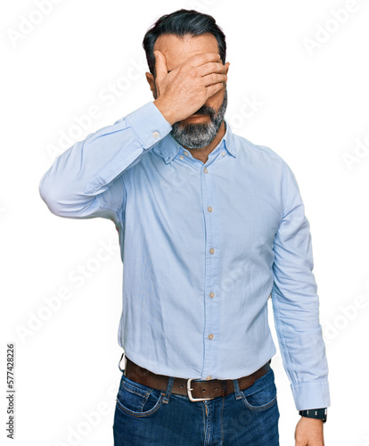 Middle aged man with beard wearing business shirt covering eyes with hand, looking serious and sad. sightless, hiding and rejection concept © Krakenimages.com