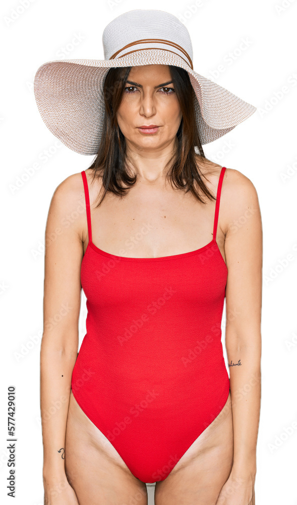 Beautiful brunette woman wearing swimsuit and summer hat skeptic and nervous, frowning upset because of problem. negative person.