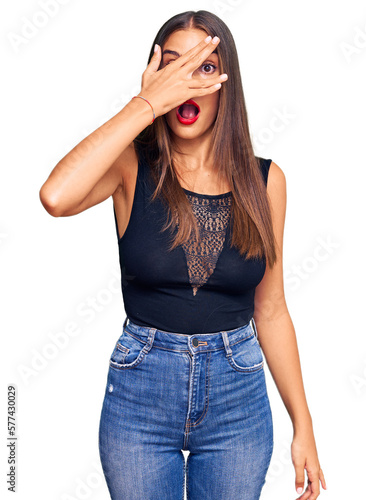 Young hispanic woman wearing casual clothes peeking in shock covering face and eyes with hand, looking through fingers with embarrassed expression.