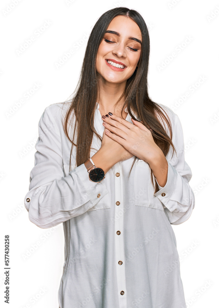 Young beautiful woman wearing casual white shirt smiling with hands on chest with closed eyes and grateful gesture on face. health concept. Young beautiful woman wearing casual white shirt smiling with hands on chest with closed eyes and grateful gesture on face. health concept.