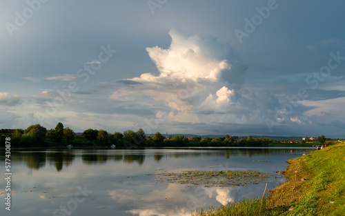 Landscape with river and sunlit big cumulonimbus cloud in sky, storm clouds and dramatic light