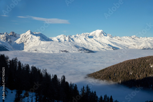 Montagnes enneigée et forêt entourées de nuages pendant l'hiver avec un ciel bleu. 