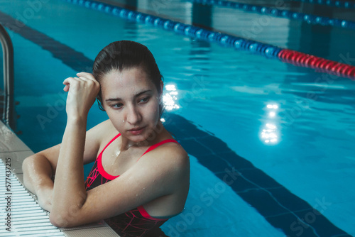 Young beautiful brunette girl on the background of the pool. Portrait of a girl near the side of the pool. Swimming  healthy lifestyle.