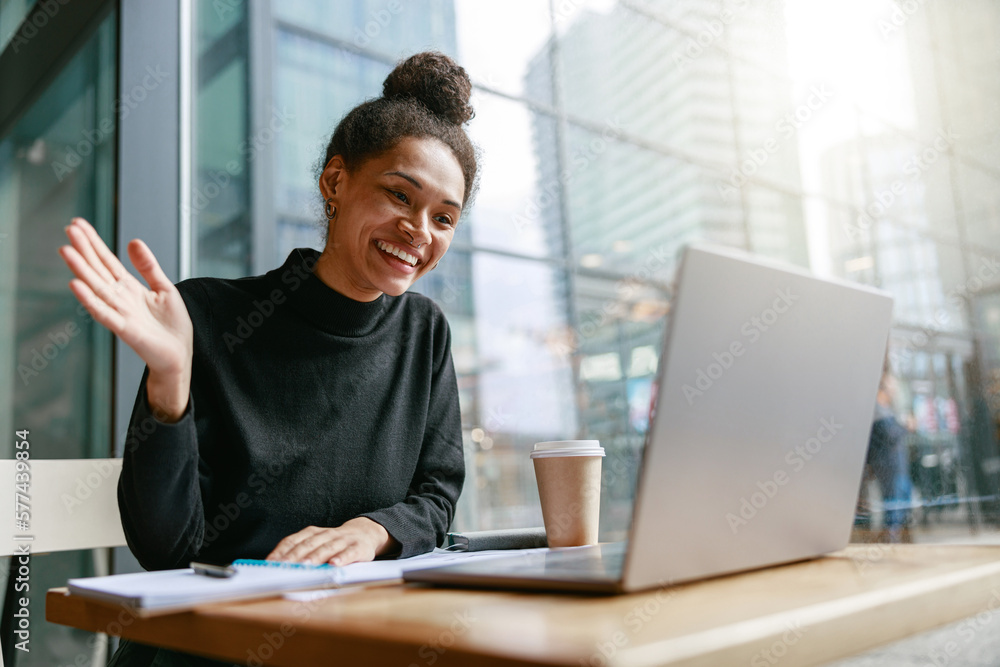 Smiling woman freelance talking with client via video call and waving Hi sitting in cafe Smiling woman freelance talking with client via video call and waving Hi sitting in cafe