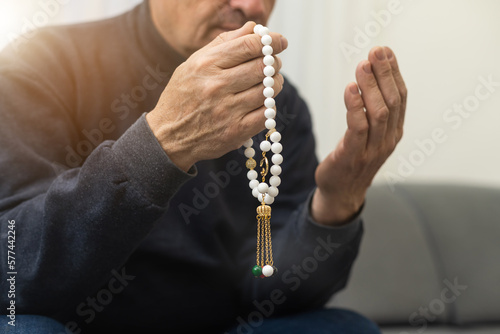 an elderly man prays with a rosary and the flag of the United Arab Emirates