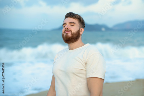 happy handsome free guy, young calm relaxed carefree man traveler enjoy sea on beach, ocean view, person feeling good, breath deep deeply fresh air. Freedom, travel, happiness concept, summer vacation