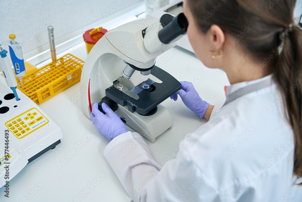Laboratory assistant examines sample biomaterial for DNA test under microscope Laboratory assistant examines sample biomaterial for DNA test under microscope