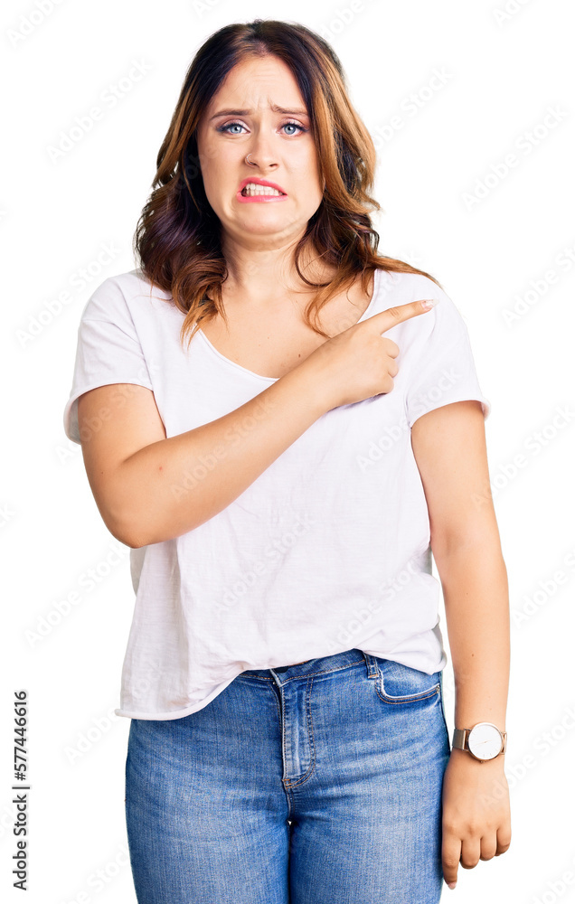 Young beautiful caucasian woman wearing casual white tshirt pointing aside worried and nervous with forefinger, concerned and surprised expression Young beautiful caucasian woman wearing casual white tshirt pointing aside worried and nervous with forefinger, concerned and surprised expression