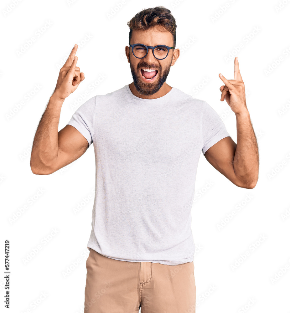 Young hispanic man wearing casual clothes and glasses shouting with crazy expression doing rock symbol with hands up. music star. heavy music concept. Young hispanic man wearing casual clothes and glasses shouting with crazy expression doing rock symbol with hands up. music star. heavy music concept.