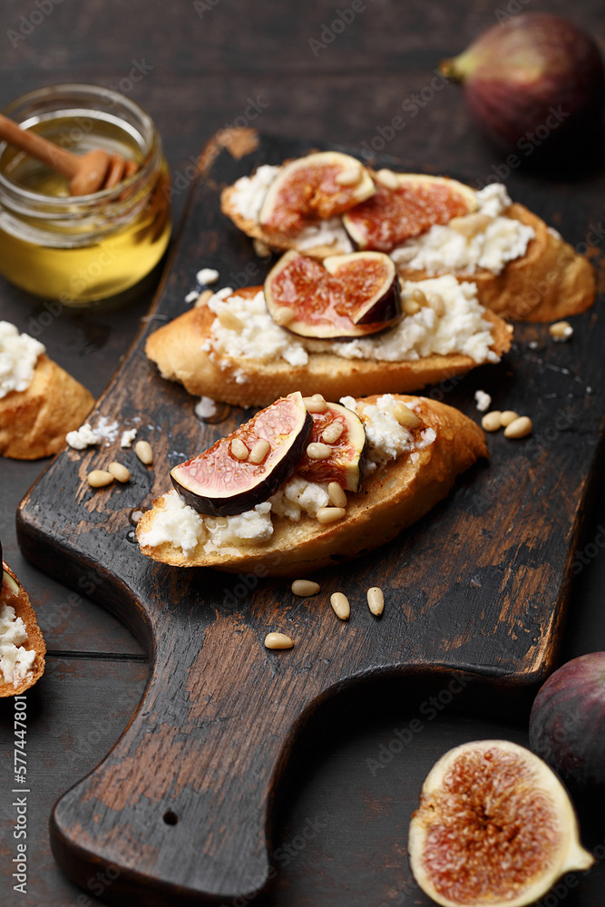 Fototapeta premium Delicious bruschetta with figs, cream cheese, pine nuts and honey on dark wooden board. Close up view, selective focus