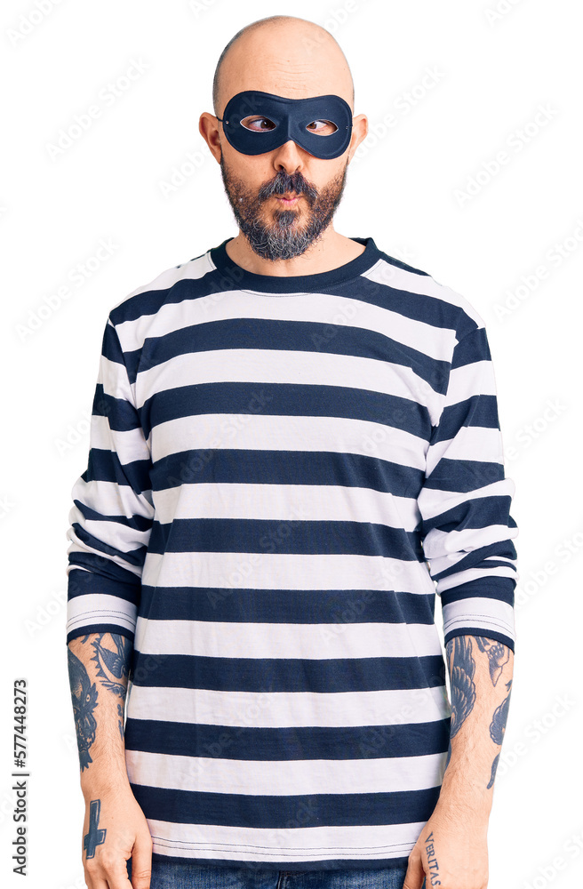 Young handsome man wearing burglar mask making fish face with lips, crazy and comical gesture. funny expression. Young handsome man wearing burglar mask making fish face with lips, crazy and comical gesture. funny expression.