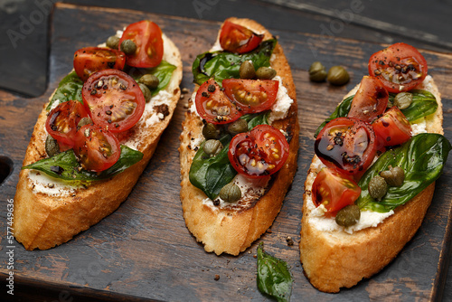 Canvas-taulu Traditional italian bruschetta with cherry tomatoes, cream cheese, basil leaves, capers and balsamic vinegar on wooden cutting board