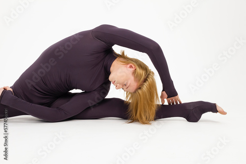 Young athletic professional ballet dancer in a black unitard is in perfect shape, performing and doing splits over a white background.