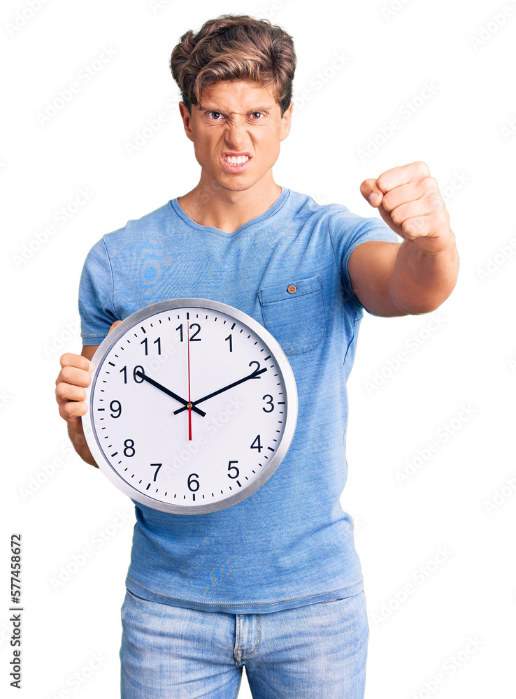 Young handsome man holding big clock annoyed and frustrated shouting with anger, yelling crazy with anger and hand raised Young handsome man holding big clock annoyed and frustrated shouting with anger, yelling crazy with anger and hand raised