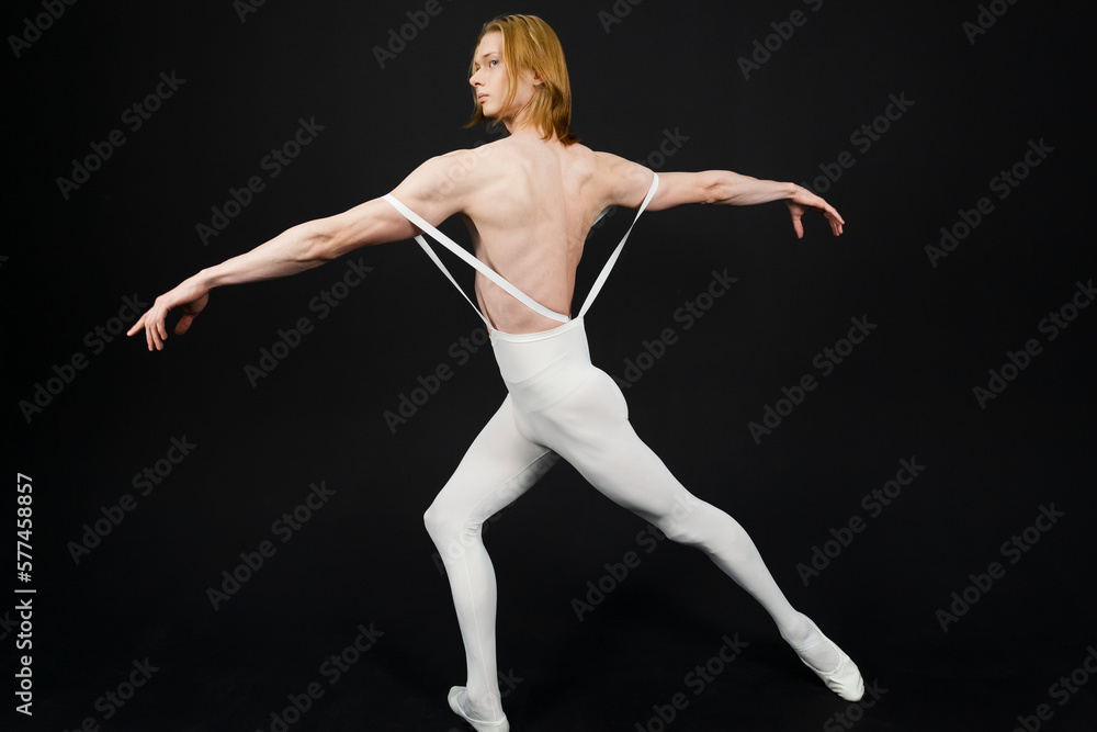 Young athletic professional ballet dancer with a bare torso and white dance tights is in perfect shape, performing and posing over a black background.