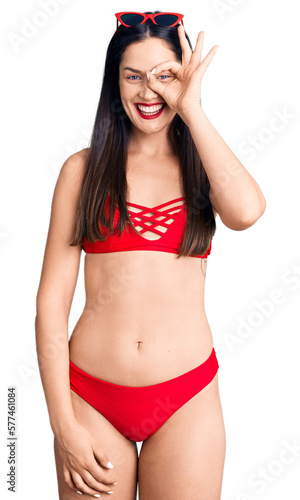 Young beautiful caucasian woman wearing bikini doing ok gesture with hand smiling, eye looking through fingers with happy face. © Krakenimages.com