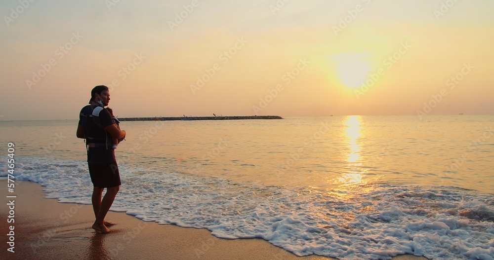 Happy Asian family father carrying embracing baby infant standing relaxing at tropical sandy Beach during Sunset shining sun with waves, Relationship, love, travel, Parenthood, vacation, summertime